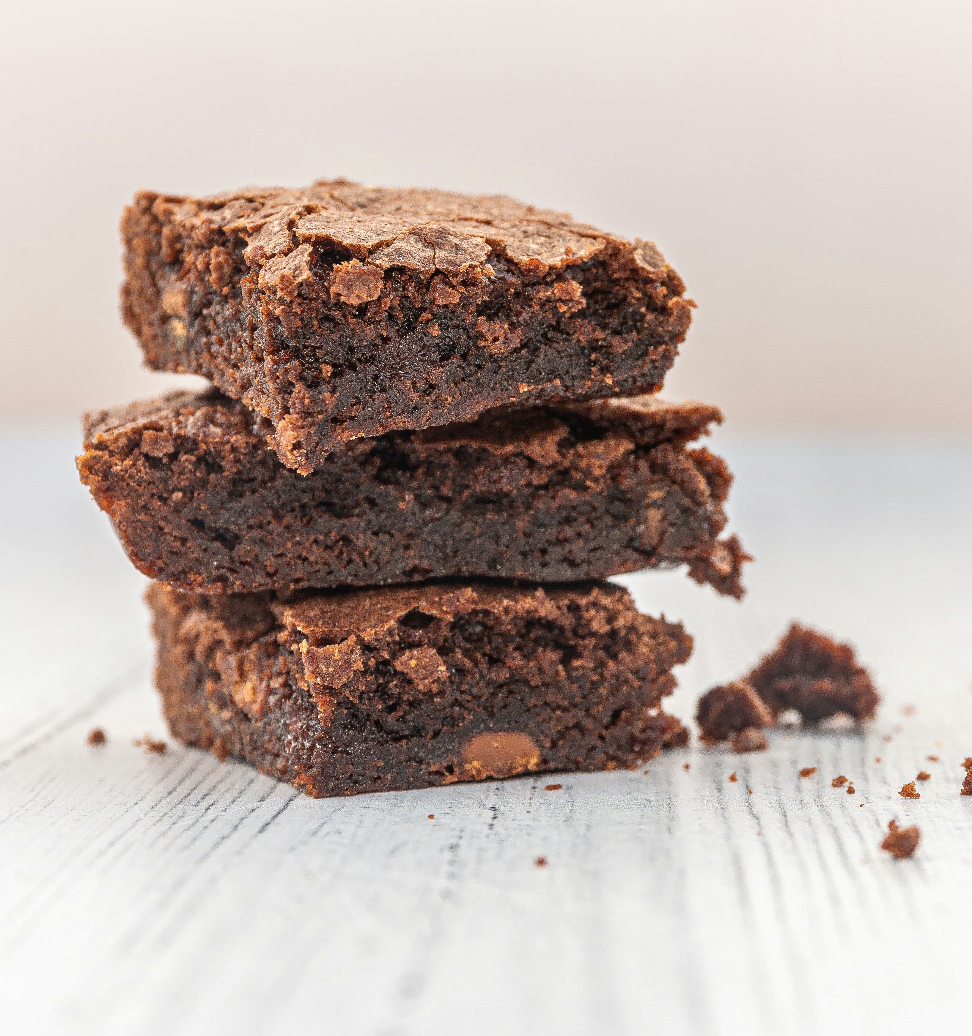 Stacked rich chocolate brownies with fudgy centres and crisp crackly tops on a white wooden table